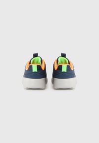 Une paire de baskets bleu marine avec des accents orange et vert néon, semelles blanches, vue de l'arrière sur un fond uni.