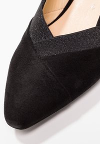 Chaussure à talon haut en suède noir avec un bout pointu et une bande élastique texturée à l'ouverture. Doublure intérieure lisse avec des accents minimalistes.