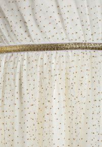Robe en tissu transparent blanc avec de petits points de paillettes dorées et une ceinture horizontale brillante dorée.