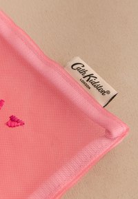 Růžová látka s texturovaným vzorem, zdobená vyšívanými detaily ve tmavší růžové barvě. Je viditelná štítek s nápisem "Cath Kidston London".