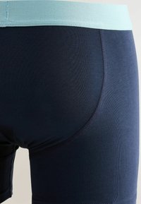 Detailný pohľad na tmavomodré boxerky s svetlomodrým pásom, ukazujúci štruktúru tkaniny a detaily šitia.