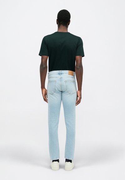 Svetlomodré džínsy s rovnými nohavicami, zadné vrecká a hnedá kožená nášivka na chrbte. Nosené s čiernym tričkom a bielymi topánkami.