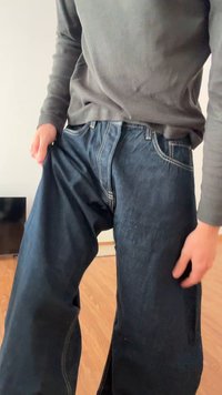 Tmavě modré džíny z denimu s kontrastním světle modrým stehováním, volným střihem a rovnou linií, držené osobou v šedém tričku s dlouhým rukávem.