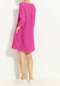 Robe en lin rose avec des manches trois-quarts, des poches latérales et une forme évasée, tombant au-dessus du genou. Des baskets blanches complètent la tenue.