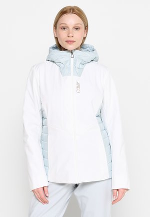 Donna che indossa una giacca invernale bianca e azzurra con zip e cappuccio, in piedi dritta su uno sfondo bianco semplice.