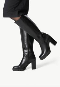 Botas de cuero negro hasta la rodilla, fabricadas en piel suave. Presentan un tacón grueso y una suela texturizada y estriada. Detalle de cremallera en el lateral.