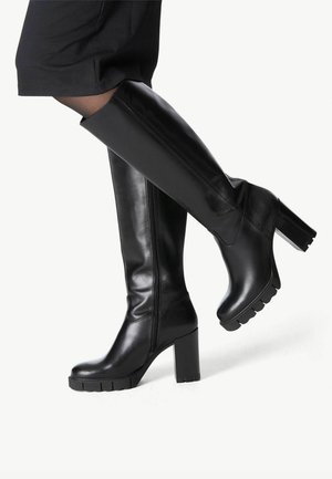 Botas de cuero negro hasta la rodilla, fabricadas en piel suave. Presentan un tacón grueso y una suela texturizada y estriada. Detalle de cremallera en el lateral.