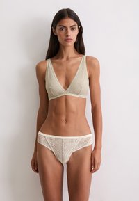 Helles beiges Bralette mit tiefem V-Ausschnitt und aufwändigem Muster; passende Bikini-Unterteile mit Details und einem weichen Bund.