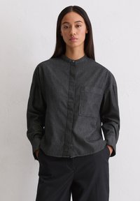 Camicia button-up grigio scuro con colletto a bandana, maniche lunghe e taschino frontale. Realizzata in un tessuto morbido con una sottile trama.