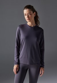 Långärmad idrottströja i mörklila tyg, rund halsringning, slät textur, matchande med åtsittande leggings.