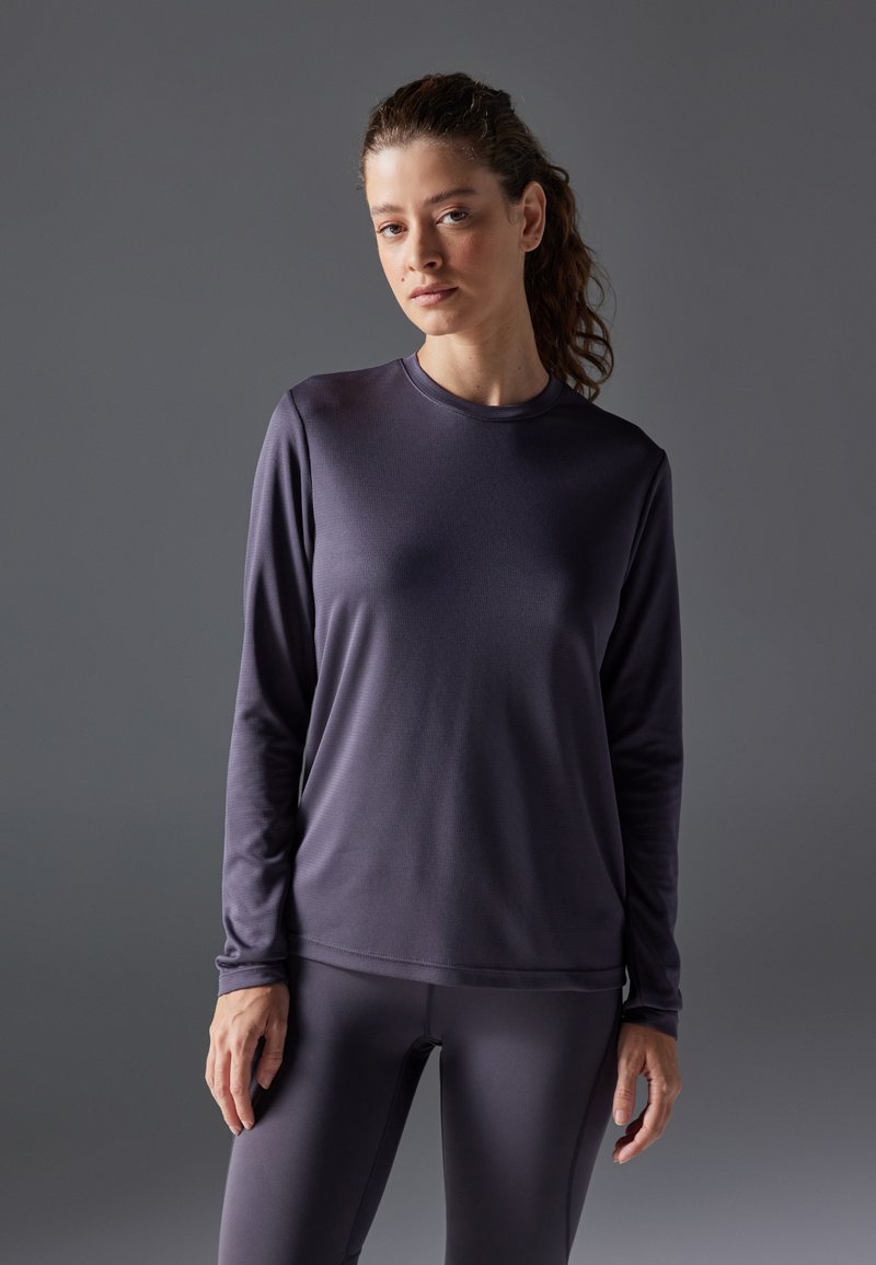 Långärmad idrottströja i mörklila tyg, rund halsringning, slät textur, matchande med åtsittande leggings.