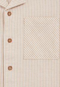 Camicia a righe in morbido beige e bianco. Presenta una tasca frontale con righe diagonali, bottoni tondi e colletto classico.
