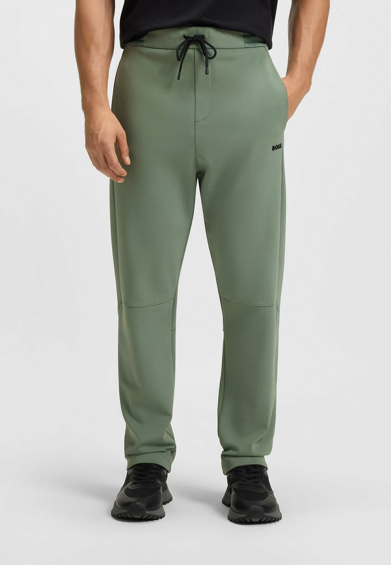 Grüne sportliche Sweatpants mit einem Kordelzugbund, Seitentaschen und einem schwarzen Logo. Glatte Stoffqualität mit passgenauer Passform und schmal zulaufenden Beinen.