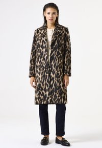 Leopardprint wollen jas met een getailleerde kraag, enkelbreasted ontwerp, twee knopen en zijzakken; gedragen over een crèmekleurige trui en donkere jeans.