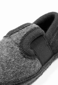 Grijze gevoerde slippers met een gestructureerde bovenkant, zwarte elastieken band en een gebogen vorm voor een eenvoudige instapstijl. Zacht, warm materiaal.