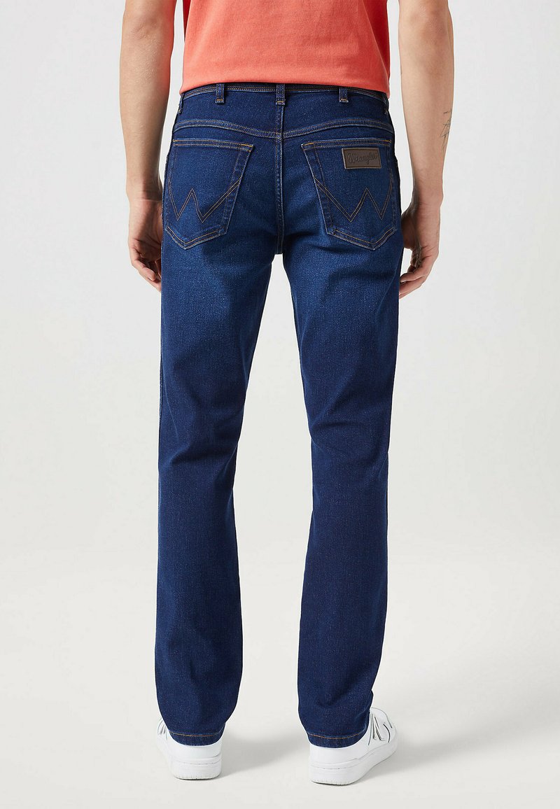 Ciemnoniebieskie dżinsy o prostym kroju, z dwiema tylnymi kieszeniami z zygzakowym ściegiem oraz brązową skórzaną metką na pasku.