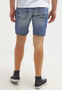 Bermudas de mezclilla en azul claro con un acabado deslavado, puños enrollados y bolsillos traseros. Combinadas con zapatillas altas negras.