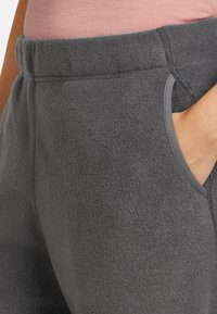 Joggers de felpa gris con bolsillos laterales, cinturilla elástica y detalles de costura en contraste. Textura suave y ajuste relajado.