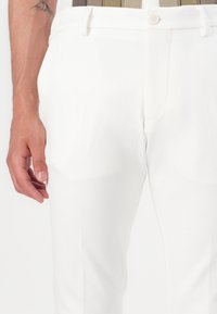 Weiße, schmal geschnittene Hose aus glattem Stoff, mit Reißverschluss und einer Vorderseite mit Tasche, ergänzt durch einen Knopfverschluss.
