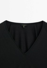 T-shirt noir à col en V avec des coutures visibles et une petite étiquette noire cousue à l'intérieur de l'encolure.