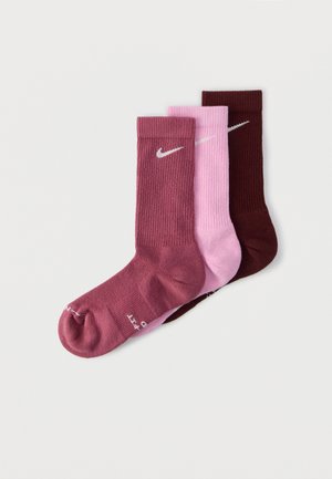 Trois chaussettes Nike crew en bordeaux, rose et marron foncé, chacune avec un logo Nike swoosh blanc près du haut du bord.