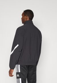 Μαύρο ελαφρύ μπουφάν με ψηλό γιακά, ελαστικές μανσέτες και λευκή ρίγα στο πλάι. Φορεμένο με μαύρο παντελόνι με λευκές ρίγες.