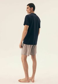 Granatowa bawełniana koszulka polo w połączeniu z szarymi szortami, o luźnym kroju i krótkich rękawach. Model stoi boso, tyłem.