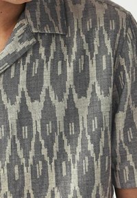 Korte mouwen shirt met een grijs en beige ikatpatroon, gemaakt van een textuurstof en ontworpen met een klassieke kraag.