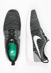 Para czarnych i szarych sneakerów Nike z białym logo swoosh, teksturowaną cholewką z dzianiny i białą, amortyzującą podeszwą, pokazana z widoków z góry i z boku.