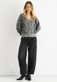 Grau leopardgemusterter Cardigan aus Strickstoff, mit tiefem V-Ausschnitt, langen Ärmeln und goldfarbenen Knöpfen. Kombiniert mit schwarzen weit geschnittenen Jeans.