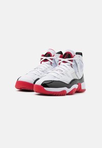 Baskets blanches de sport avec des accents en cuir verni noir, des semelles rouges et un dessus en tissu texturé présentant des détails de logo circulaires au niveau de la cheville.