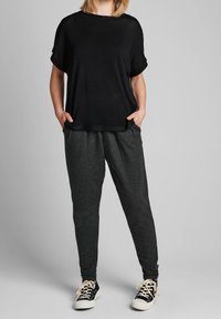 Schwarzes T-Shirt mit umgeschlagenen Ärmeln, kombiniert mit dunkelgrauen Jogginghosen und schwarzen Sneakers mit weißen Akzenten. Leger, entspannte Passform.