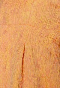 Tecido laranja texturizado com uma aparência amarrotada; apresenta pregas e um brilho sutil. O material tem ligeiras variações na intensidade da cor.