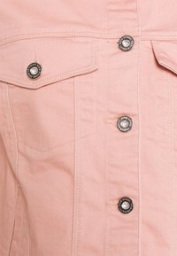 Tela de mezclilla rosa claro con un diseño abotonado con botones de metal y dos bolsillos frontales, destacando una superficie texturizada y resistente.