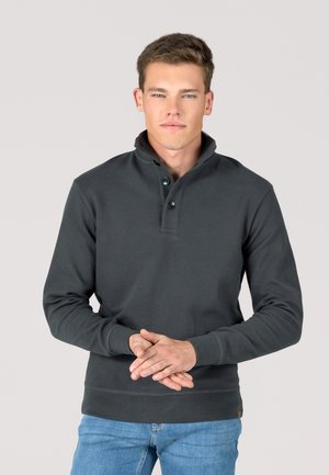 Dunkelgrauer Pullover mit Kragen und dreiknöpfiger Leiste, gerippter Textur und langen Ärmeln. Kombiniert mit hellblauen Jeans.