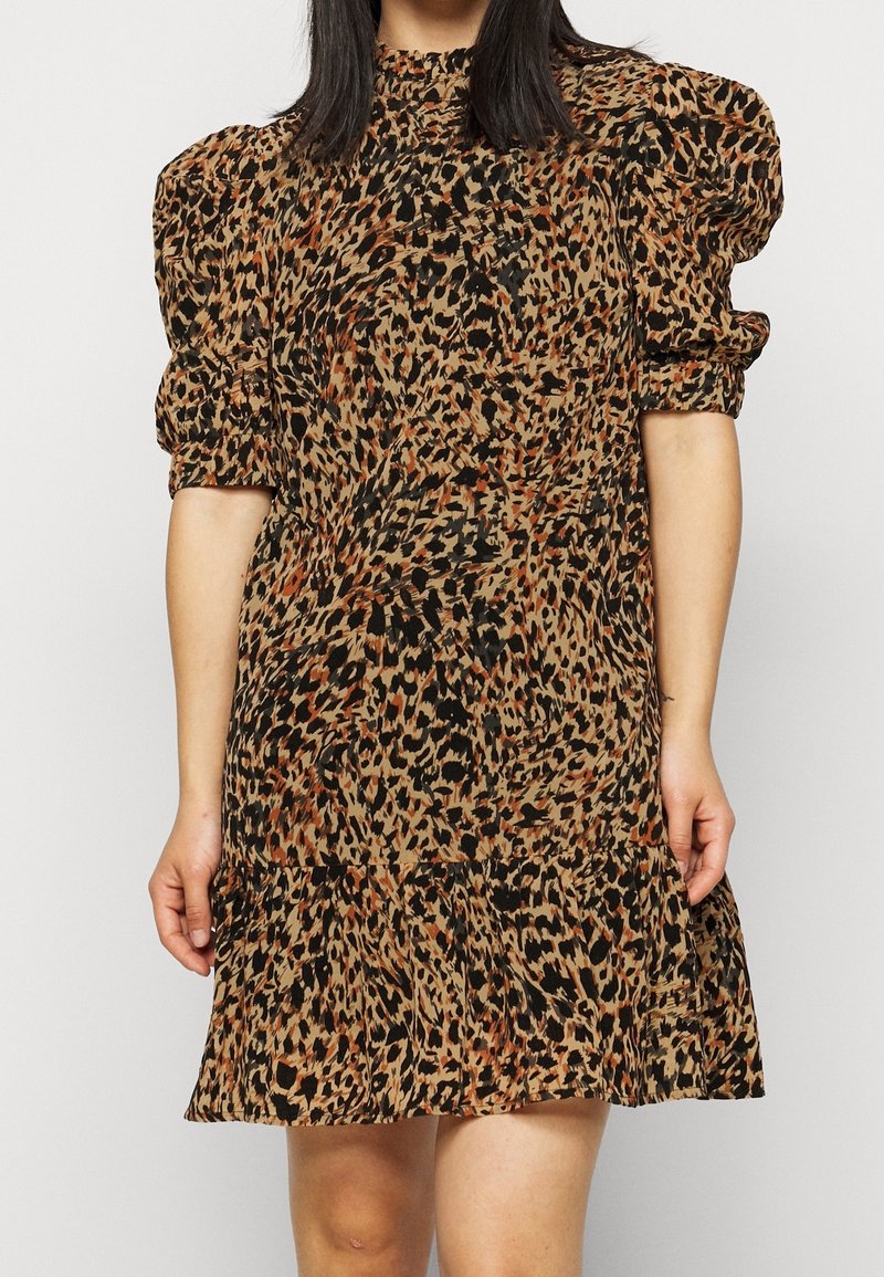 Eläinkuosilla varustettu mekko, jossa on puffihihat, korkea kaula-aukko ja levenevä hame. Värit ovat beige, musta ja ruskea oransseilla yksityiskohdilla.