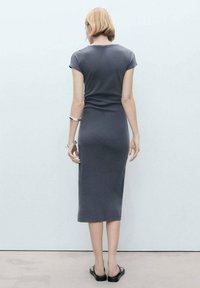 Robe midi grise ajustée avec des manches courtes, texture lisse et design simple. Portée avec des sandales noires et un bracelet en argent au poignet.