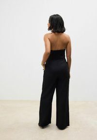 Nadette noire sans manches avec un corsage froncé, des jambes larges et une finition de tissu lisse. Présente une silhouette épurée et une élégance décontractée.