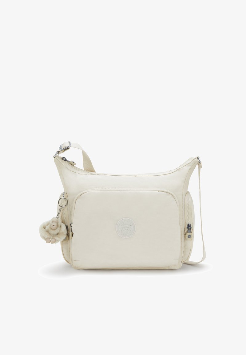 Beżowa torebka na ramię z przednią kieszenią, regulowanym paskiem, bocznymi kieszeniami na zamek oraz małym pluszowym breloczkiem w kształcie małpki.