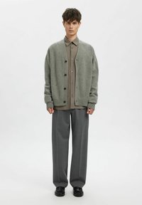 Gaiši pelēks adīts kardigans ar brīvu piegriezumu, melnām pogām. Kombinēts ar rūtainu kreklu ar pogām un pelēnām platajam kāju biksēm.