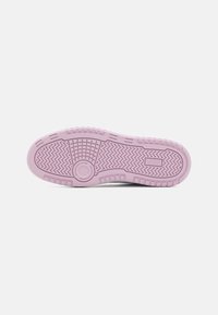 Suela de zapatilla que presenta un material de goma rosa, un patrón de relieve texturizado con diseños circulares y en zigzag, y un detalle de marca.