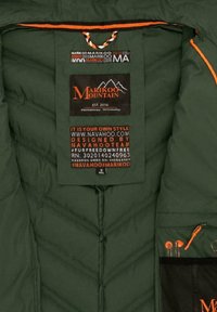 Grön isolerad jacka inuti med sicksack-quilting, orange detaljer och flerfaldiga märken som visar skötselråd och storlekar.