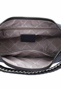 Interno di una borsa in denim blu con fodera grigia a motivo, tasca con zip e etichetta del logo. Presente anche un dettaglio della tracolla a catena e intrecciata.