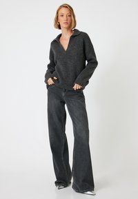 Maglione a coste grigio scuro con scollo a V e colletto, abbinato a jeans in denim scuro a vita alta e gamba larga. Calzature lisce e eleganti.