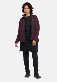 Fleece jacket in dark purple with black trim, layered over a black dress and quilted skirt. Black leggings and boots complete the outfit.