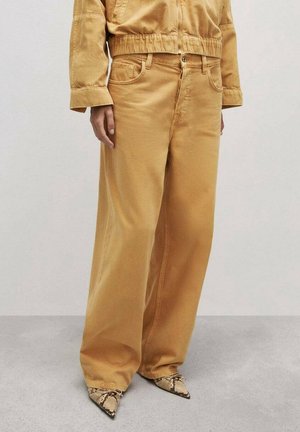 Szerokie spodnie w kolorze musztardowym połączone z wężowymi butami na szpic oraz pasującą krótką kurtką z długimi rękawami.