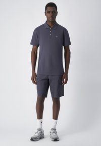 Granatowa koszulka polo z kołnierzykiem i trzema guzikami, zestawiona z granatowymi spodenkami cargo. Stylizowana z białymi skarpetkami ściągaczowymi i szarymi trampkami.