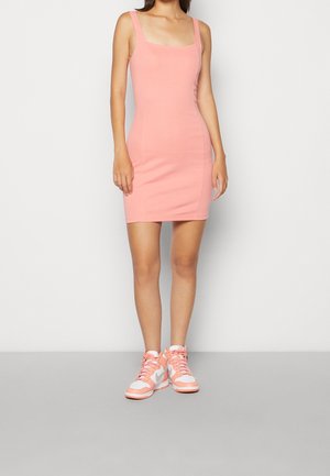 Robe bodycon rose à encolure carrée, avec des bretelles minimalistes. Associée à des baskets montantes roses claires avec des accents et des lacets blancs.