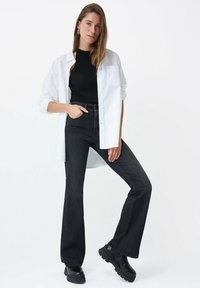 Chemise blanche à boutons sur un débardeur noir en côte, associée à un jean noir en denim taille haute évasé et des bottes noires imposantes.