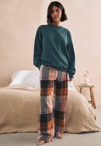 Teal sweatshirt med rund hals, parret med plaid bukser med brede ben i nuancer af orange, grå og pink. Bløde strukturer er synlige.